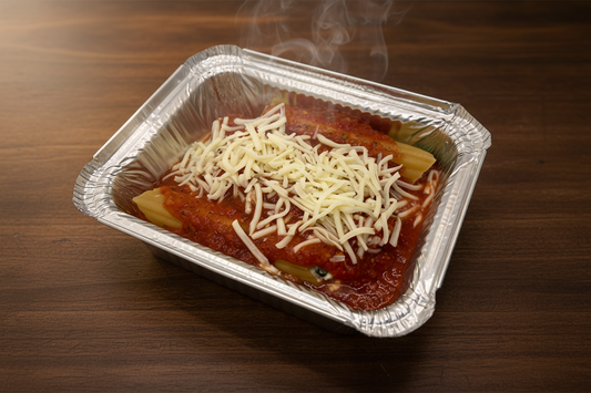 A foil tray containing uncooked stuffed shells or manicotti pasta with a topping of shredded cheese.